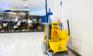 Cleaning on university campuses: Custodial cart with yellow caution floor is wet signs, bucket and mop sitting on a tile floor outside of a college/university library